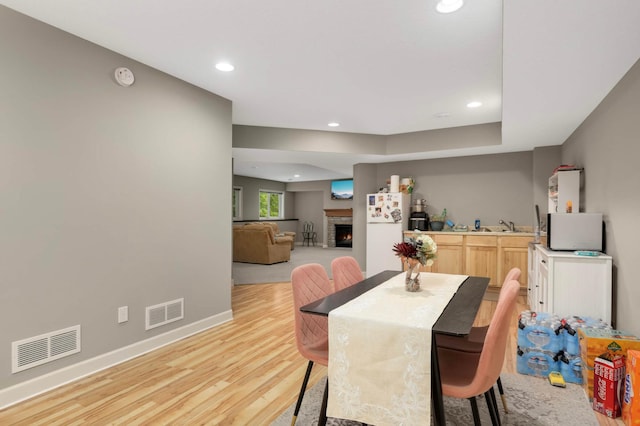 11950 75th St NE, Otsego, MN 55301 - dining room featuring light wood-style floors, recessed lighting, a warm lit fireplace, and bar with sink