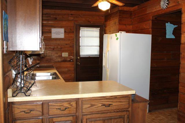 47393 209th Pl, Mcgregor, MN 55760 - kitchen with white fridge with ice dispenser, ceiling fan, wooden walls, light countertops, and a peninsula