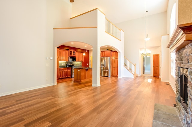 10725 Toledo Ln N, Brooklyn Park, MN 55443 - unfurnished living room featuring a towering ceiling, a fireplace, light wood-style flooring, a chandelier, and arched walkways