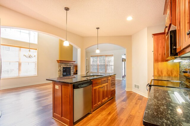 10725 Toledo Ln N, Brooklyn Park, MN 55443 - kitchen featuring dishwasher, arched walkways, a stone fireplace, light wood-style floors, and dark stone countertops