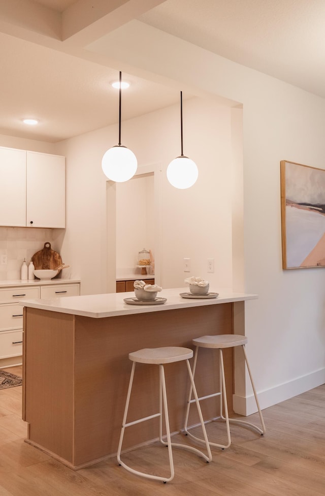 212 Diamond Lake Rd, Minneapolis, MN 55419 - kitchen featuring a kitchen bar, white cabinets, light countertops, light wood finished floors, and hanging light fixtures