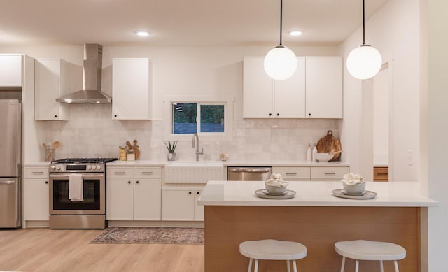 212 Diamond Lake Rd, Minneapolis, MN 55419 - kitchen with wall chimney exhaust hood, stainless steel appliances, a breakfast bar area, light wood-style flooring, and white cabinets