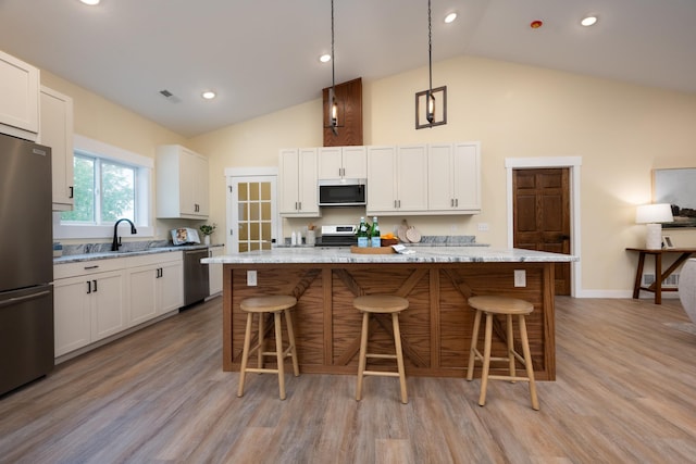 kitchen with appliances with stainless steel finishes, high vaulted ceiling, a breakfast bar, light wood-type flooring, and white cabinets