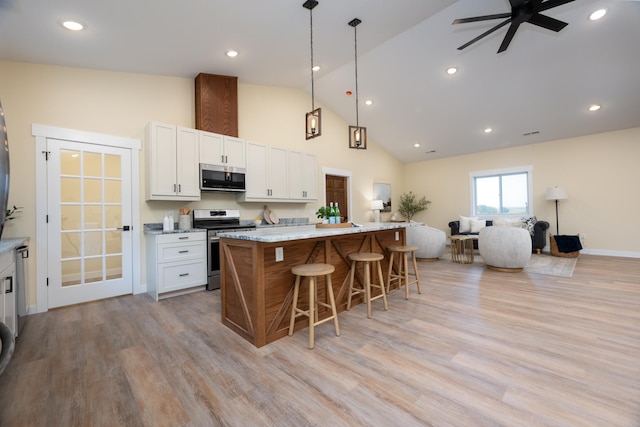 kitchen featuring stainless steel appliances, a kitchen bar, open floor plan, white cabinetry, and high vaulted ceiling
