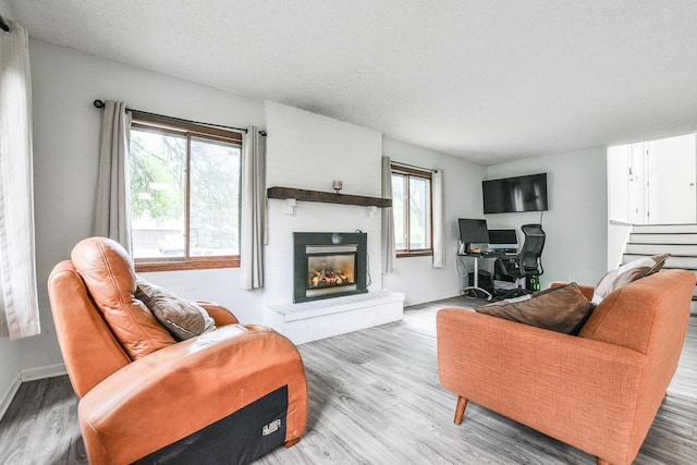 7097 Robinwood Bay, Woodbury, MN 55125 - living room featuring a brick fireplace, healthy amount of natural light, wood finished floors, stairs, and a textured ceiling