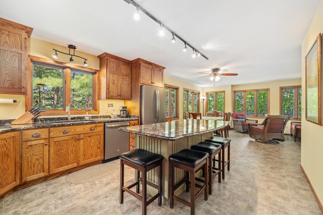 23148 Glenhaven Dr, Nevis, MN 56467 - kitchen featuring appliances with stainless steel finishes, a kitchen breakfast bar, brown cabinetry, dark stone counters, and a ceiling fan