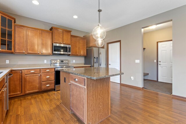 17393 54th St NE, Otsego, MN 55374 - kitchen featuring stainless steel appliances, wood finished floors, a center island, brown cabinets, and glass insert cabinets