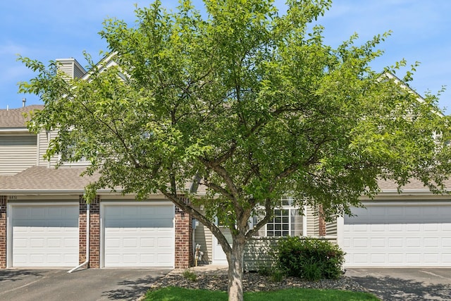 8829 Branson Dr Unit 46, Inver Grove Heights, MN 55076 - view of property hidden behind natural elements with brick siding, a garage, a shingled roof, and driveway