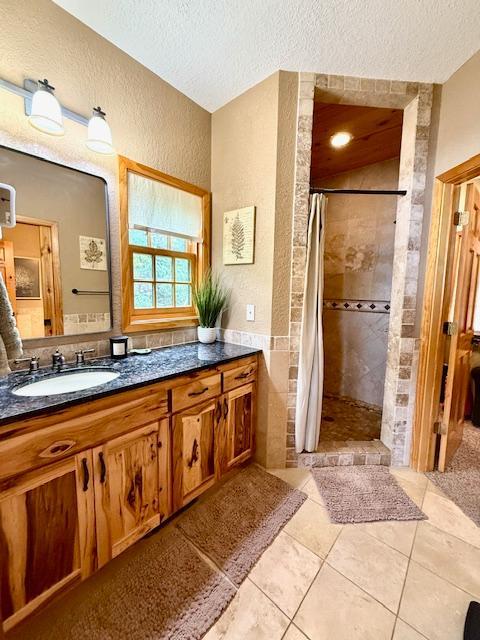 49512 202nd Pl, Shamrock Twp, MN 55760 - bathroom featuring a textured ceiling, a tile shower, vanity, a textured wall, and tile patterned flooring