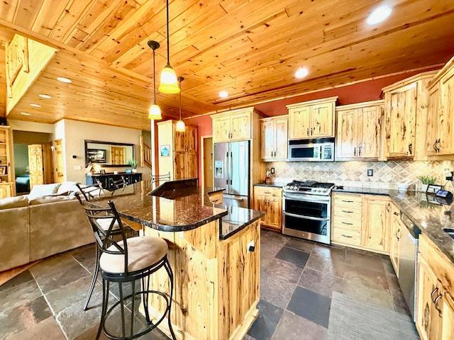 49512 202nd Pl, Shamrock Twp, MN 55760 - kitchen with appliances with stainless steel finishes, wooden ceiling, a kitchen breakfast bar, stone tile floors, and backsplash