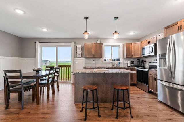 2105 Elk Run Dr SE, Pine Island, MN 55963 - kitchen featuring appliances with stainless steel finishes, a kitchen island, a wainscoted wall, a breakfast bar area, and light stone countertops