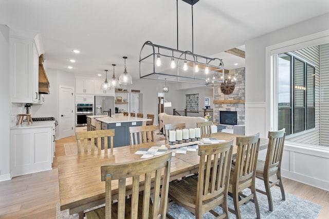 4452 167th Ave NW, Andover, MN 55304 - dining area featuring light wood finished floors, a stone fireplace, a decorative wall, a chandelier, and wainscoting