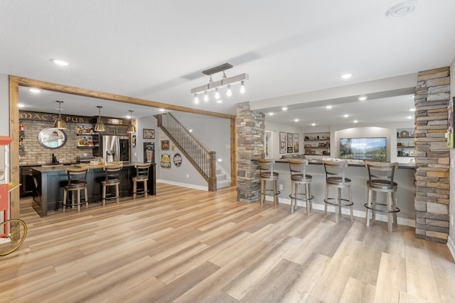 4452 167th Ave NW, Andover, MN 55304 - kitchen featuring stainless steel fridge, a breakfast bar, decorative columns, light wood-type flooring, and decorative light fixtures