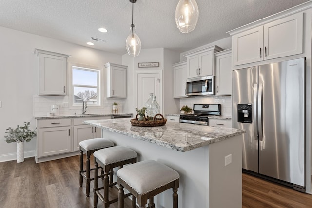 1418 Cedar Ln, Litchfield, MN 55355 - kitchen with appliances with stainless steel finishes, a kitchen island, a textured ceiling, tasteful backsplash, and a breakfast bar