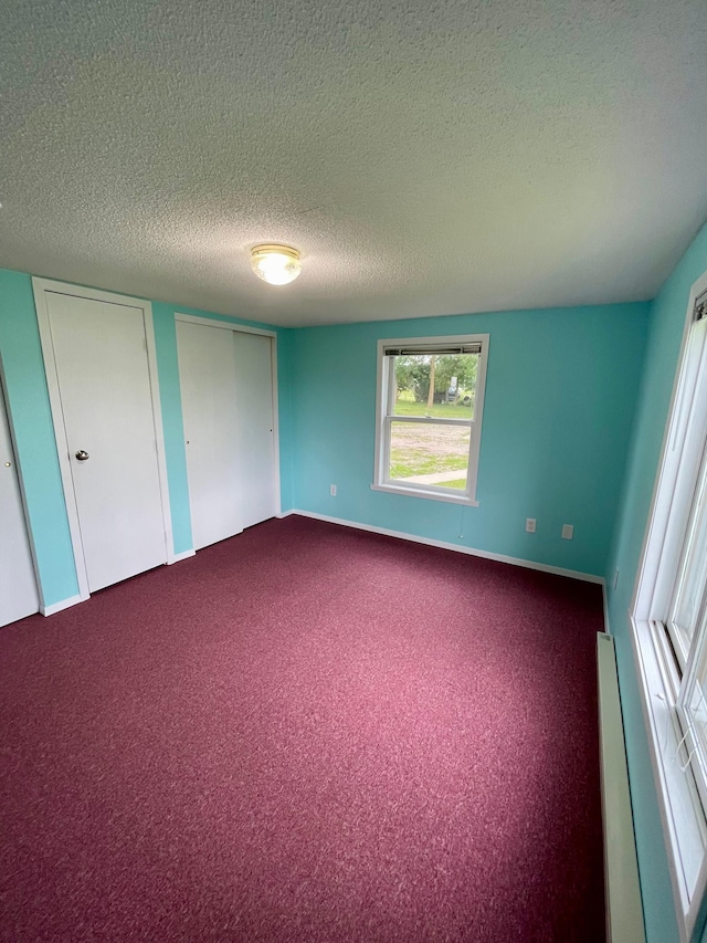 10244 State Highway 87, Blueberry Twp, MN 56464 - unfurnished bedroom with a textured ceiling, dark carpet, multiple closets, and a baseboard heating unit