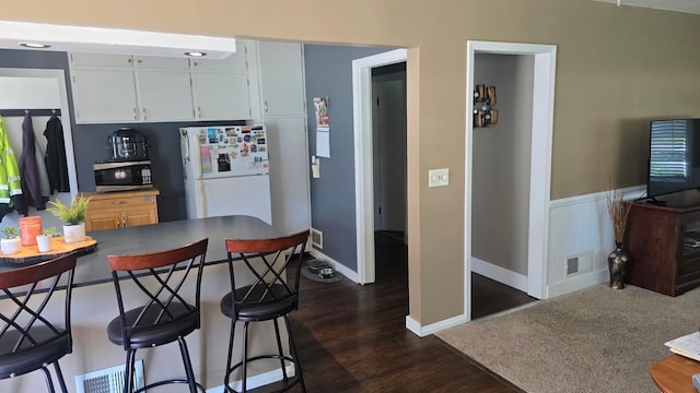 524 1st Ave SE, Wells, MN 56097 - kitchen with stainless steel microwave, freestanding refrigerator, a breakfast bar area, dark wood-style floors, and a wainscoted wall