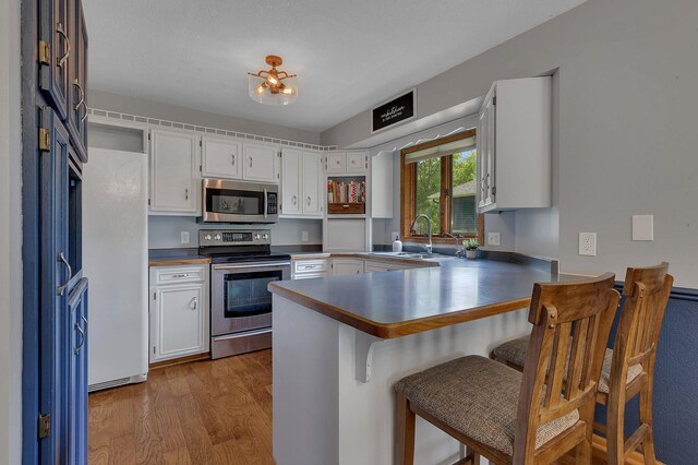 1805 7th Ave N, Sartell, MN 56377 - kitchen featuring appliances with stainless steel finishes, a peninsula, wood finished floors, white cabinetry, and a kitchen bar