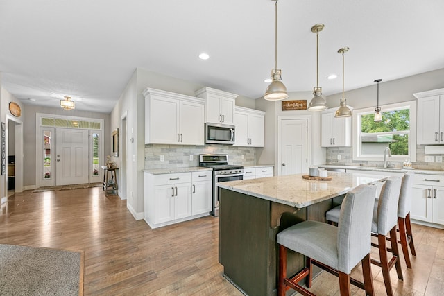19550 Albany Cir NW, Elk River, MN 55330 - kitchen with stainless steel appliances, a center island, white cabinetry, wood finished floors, and recessed lighting