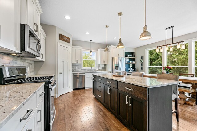 19550 Albany Cir NW, Elk River, MN 55330 - kitchen featuring stainless steel appliances, white cabinetry, a kitchen bar, tasteful backsplash, and hardwood / wood-style floors
