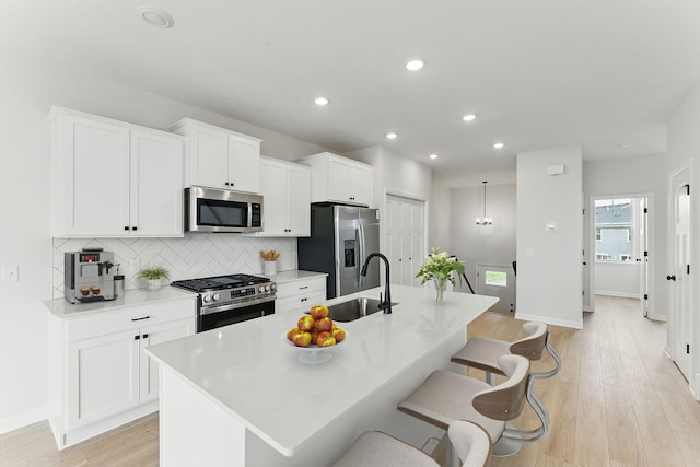 2726 Kepler Ave NE, Saint Michael, MN 55376 - kitchen with stainless steel appliances, an island with sink, light wood-style flooring, tasteful backsplash, and white cabinets