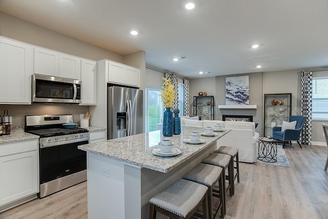 6574 208th St W, Farmington, MN 55024 - kitchen with appliances with stainless steel finishes, light wood-style floors, a kitchen island, light stone countertops, and white cabinets