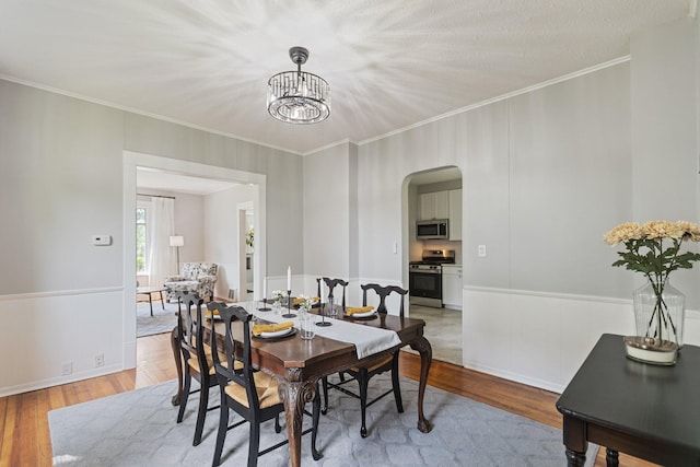 810 7th St NW, Faribault, MN 55021 - dining area with arched walkways, a chandelier, light wood-style flooring, ornamental molding, and a wainscoted wall