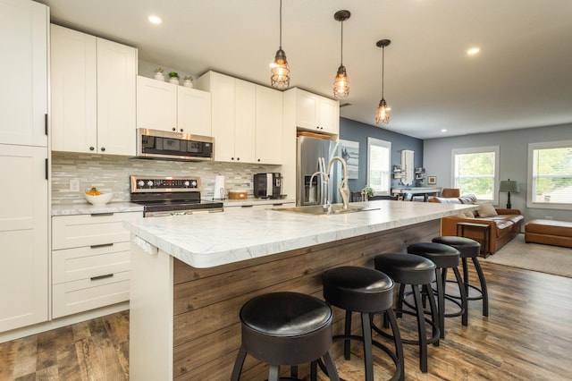 202 Park St, Alexandria, MN 56308 - kitchen with appliances with stainless steel finishes, open floor plan, dark wood finished floors, an island with sink, and white cabinetry