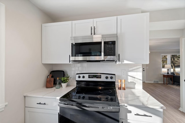 401 Plymouth Rd, Minnetonka, MN 55305 - kitchen featuring stainless steel microwave, electric range, light wood-style flooring, decorative backsplash, and white cabinets