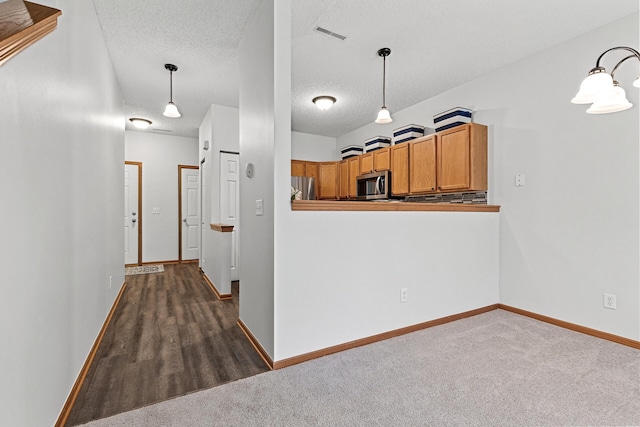 1587 Liberty St, Shakopee, MN 55379 - kitchen featuring stainless steel appliances, brown cabinets, a textured ceiling, decorative light fixtures, and dark colored carpet