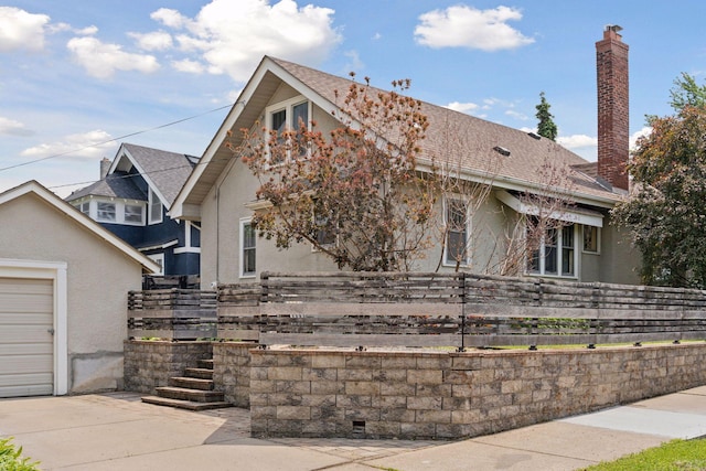 720 40th St, Minneapolis, MN 55409 - view of front facade featuring stucco siding, a chimney, a garage, roof with shingles, and driveway