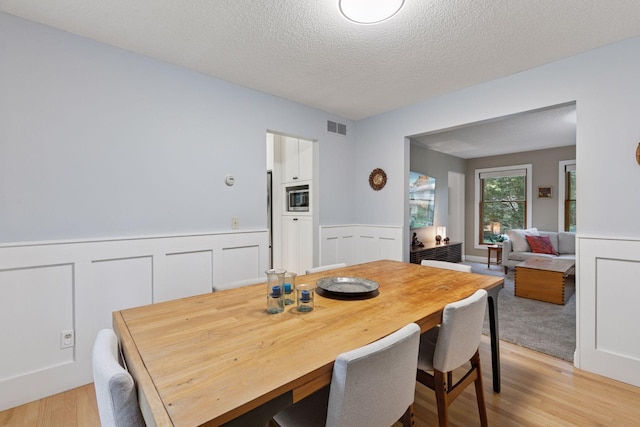 17233 Harrington Way, Lakeville, MN 55044 - dining room featuring light wood-style floors, wainscoting, a textured ceiling, and a decorative wall