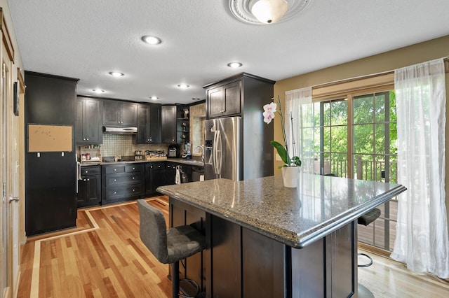 13591 347th St, Chisago Lake Twp, MN 55045 - kitchen with stainless steel fridge with ice dispenser, under cabinet range hood, a breakfast bar, light wood-type flooring, and a textured ceiling
