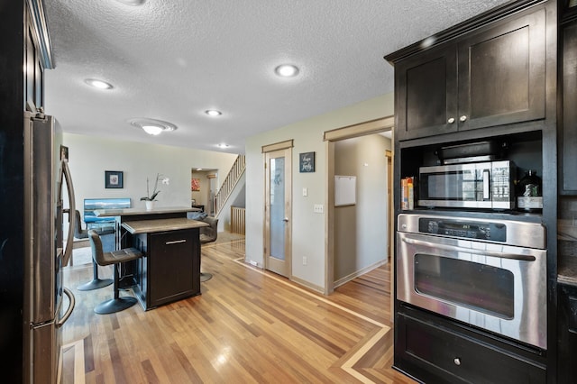 13591 347th St, Chisago Lake Twp, MN 55045 - kitchen featuring stainless steel appliances, light wood finished floors, a textured ceiling, a kitchen bar, and a center island
