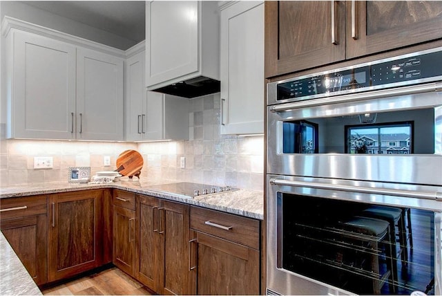 117 Maple Ct, Cannon Falls, MN 55009 - kitchen with stainless steel double oven, white cabinets, tasteful backsplash, light stone counters, and light wood-style floors