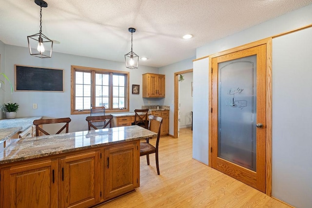 1008 3rd St NE, New Prague, MN 56071 - kitchen featuring brown cabinetry, light wood-style floors, light stone countertops, hanging light fixtures, and recessed lighting