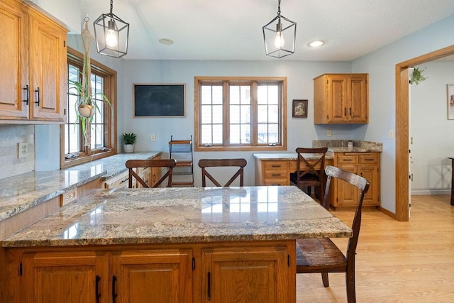 1008 3rd St NE, New Prague, MN 56071 - kitchen featuring light wood-style flooring, brown cabinetry, light stone countertops, hanging light fixtures, and recessed lighting