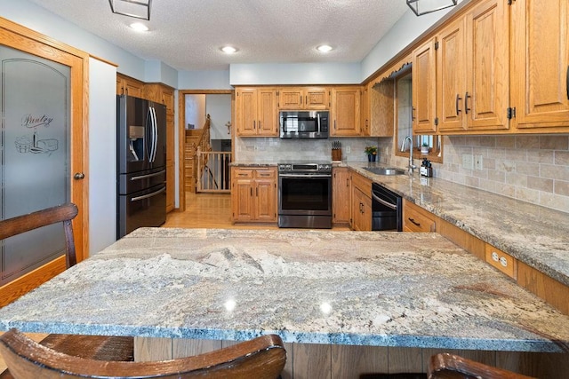 1008 3rd St NE, New Prague, MN 56071 - kitchen featuring stainless steel appliances, light stone counters, decorative backsplash, a textured ceiling, and brown cabinetry