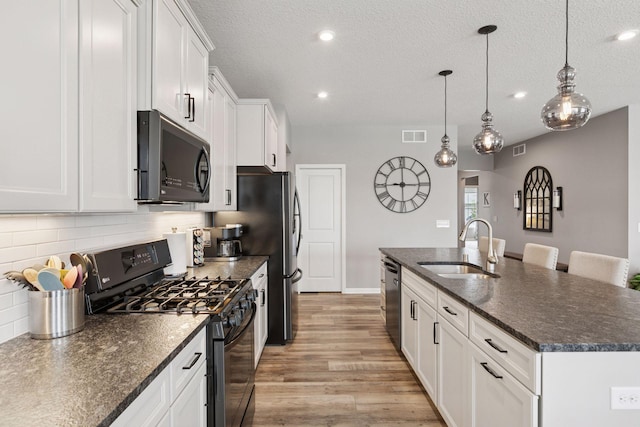 15382 71st St NE, Otsego, MN 55330 - kitchen with black range with gas cooktop, a center island with sink, light wood-style flooring, white cabinetry, and decorative backsplash