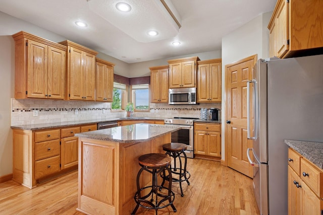 9015 Schutte Ct, Corcoran, MN 55340 - kitchen with stainless steel appliances, light wood-style floors, a kitchen bar, a center island, and light stone counters