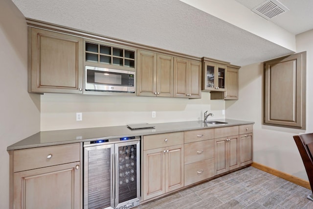 9015 Schutte Ct, Corcoran, MN 55340 - kitchen with wine cooler, stainless steel microwave, light brown cabinetry, and a textured ceiling