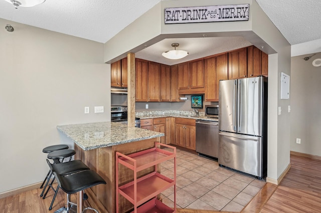 78 10th St E Unit 2901, Saint Paul, MN 55101 - kitchen with stainless steel appliances, a textured ceiling, a peninsula, brown cabinetry, and light stone countertops