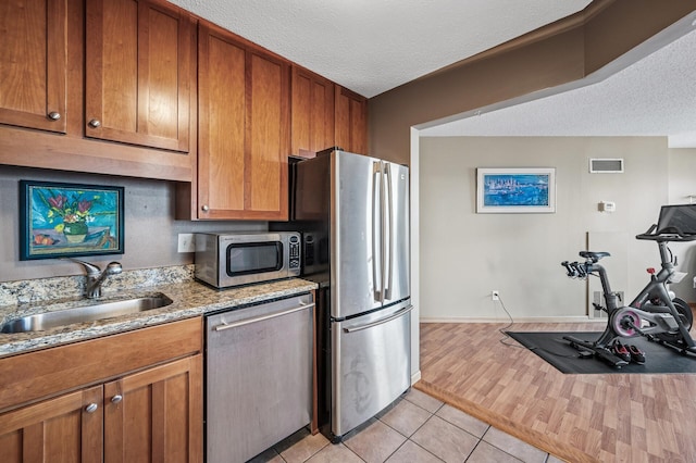 78 10th St E Unit 2901, Saint Paul, MN 55101 - kitchen with appliances with stainless steel finishes, a textured ceiling, light tile patterned flooring, brown cabinets, and light stone countertops