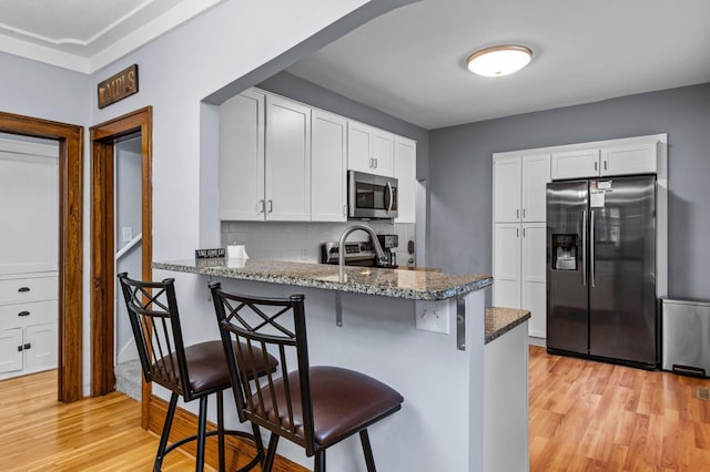 242 Winona St W, West Saint Paul, MN 55118 - kitchen with stainless steel appliances, light wood-style floors, dark stone countertops, a peninsula, and a breakfast bar area