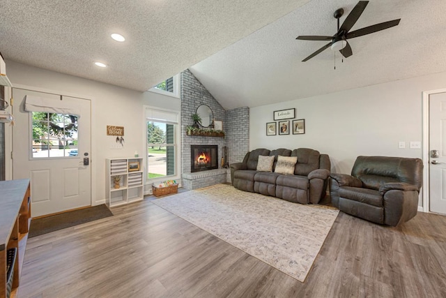2585 3rd Ave NE, Owatonna, MN 55060 - living area with a brick fireplace, a textured ceiling, wood finished floors, vaulted ceiling, and ceiling fan
