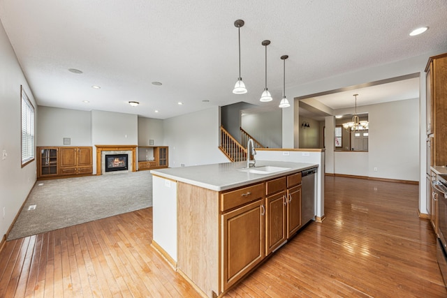 6773 Urbandale Ln N, Maple Grove, MN 55311 - kitchen featuring light wood-type flooring, a glass covered fireplace, dishwasher, a kitchen island with sink, and pendant lighting