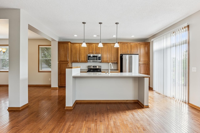 6773 Urbandale Ln N, Maple Grove, MN 55311 - kitchen featuring appliances with stainless steel finishes, light countertops, light wood-style flooring, brown cabinetry, and pendant lighting