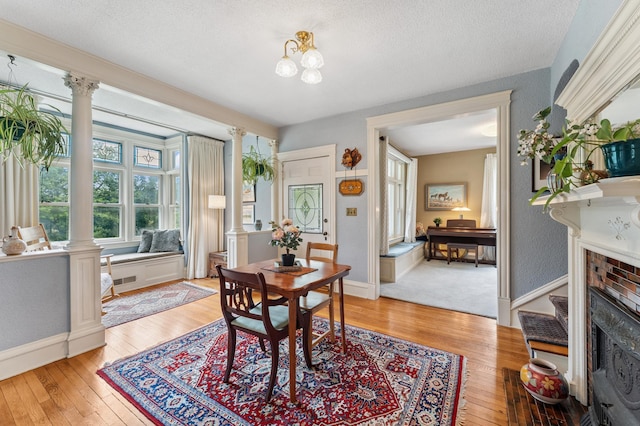 2145 Knapp St, Saint Paul, MN 55108 - dining area with ornate columns, light wood-style flooring, a brick fireplace, and a textured ceiling