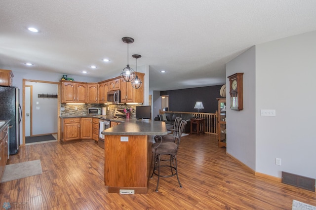 633 Leonards Way, Argusville, ND 58005 - kitchen with appliances with stainless steel finishes, a peninsula, wood finished floors, dark countertops, and brown cabinetry