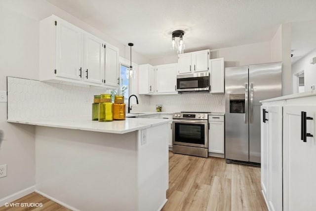 9019 Idaho Ave N, Brooklyn Park, MN 55445 - kitchen featuring appliances with stainless steel finishes, a peninsula, light wood finished floors, tasteful backsplash, and white cabinetry