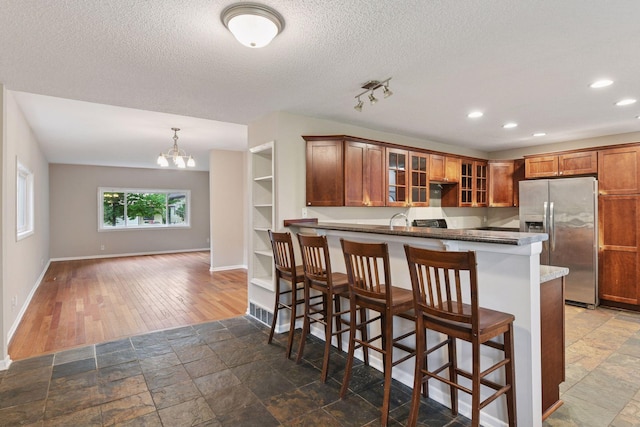 724 Pierce St NE, Minneapolis, MN 55413 - kitchen with stainless steel fridge with ice dispenser, glass insert cabinets, a kitchen bar, a chandelier, and a textured ceiling